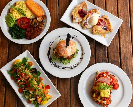 Breakfast spread of big breakfast, burger, salad, eggs benedict and a fruit galette on a timber table